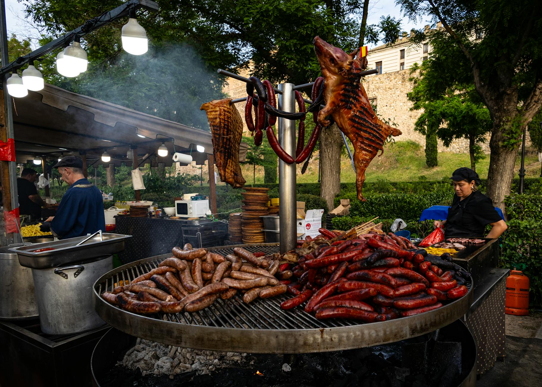 Mercado de comida al aire libre con salchichas a la parrilla y un cerdo asado, donde los chefs preparan los platos.